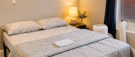 Un lit double avec une couvre-lit à motifs, une lampe de chevet, un luminaire fixé au mur et une fenêtre avec des rideaux.