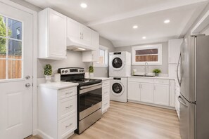 Une cuisine moderne avec des meubles blancs, des appareils électroménagers en acier inoxydable et un plancher en bois.