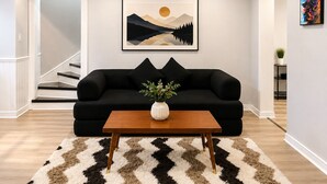 A living room with a black sofa, a wooden coffee table, and a framed landscape painting on the wall.