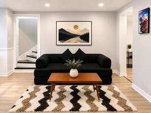 Un salon avec un canapé noir, une table basse en bois et un tableau représentant un paysage, encadré et accroché au mur.