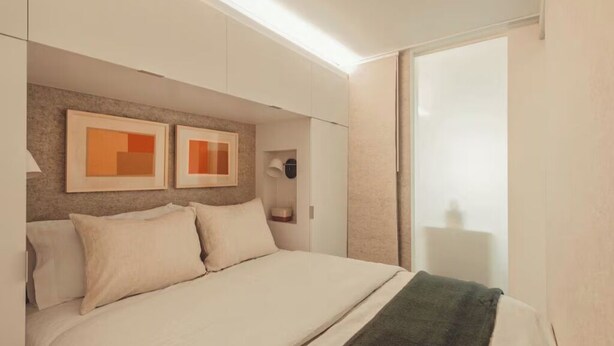 A modern bedroom with a bed, a nightstand, and a wall-mounted lamp. - Premium Studio City View w/ Kitchen, Heated Rooftop Pool & Gym | Near Midtown (Atlanta)