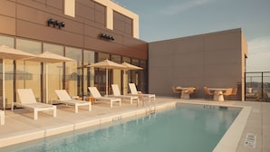 A rooftop pool area with lounge chairs and umbrellas, a pool with a clear blue water, and a modern building facade. - Premium Studio City View w/ Kitchen, Heated Rooftop Pool & Gym | Near Midtown (Atlanta)