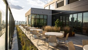 Une terrasse extérieure avec des tables et des chaises rondes, une plateforme en bois et une vue sur les toits de la ville.