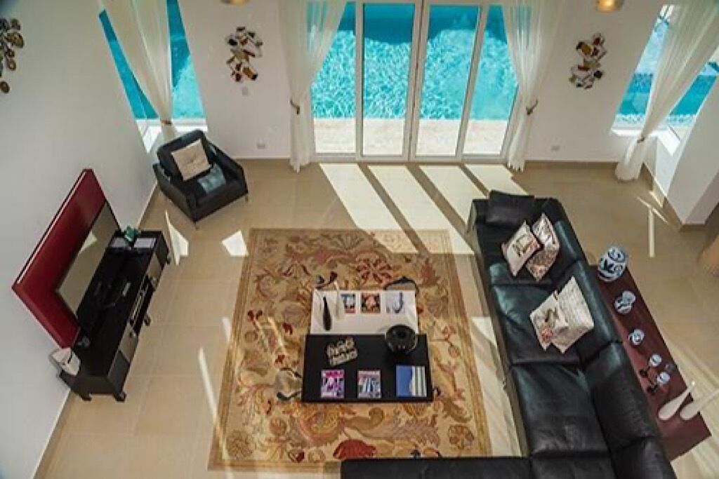 A living room with a sofa, a coffee table with magazines, and a view of a pool through large windows.