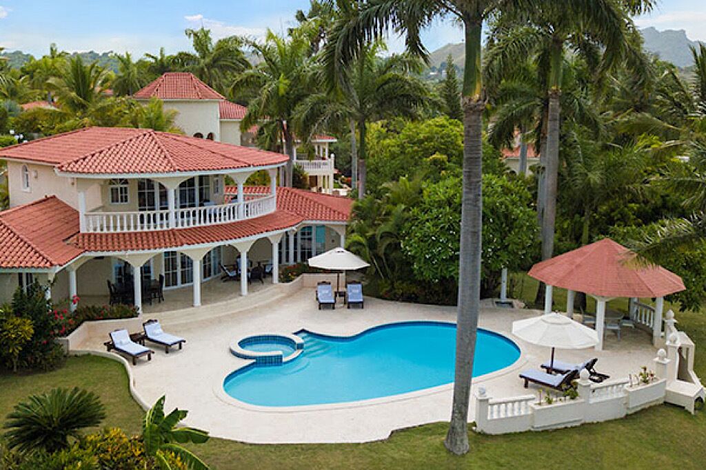 A large house with a swimming pool, multiple lounge chairs, and a covered patio area.