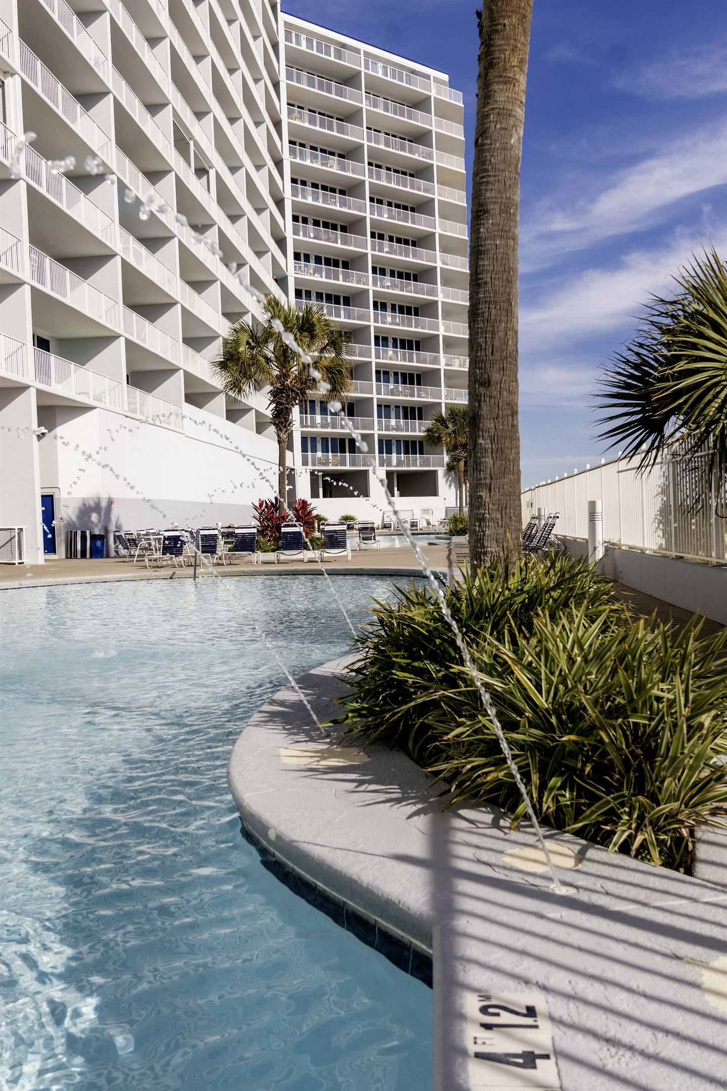 A hotel with a swimming pool, palm trees, and a modern building with balconies.