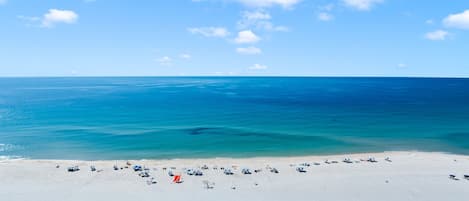 A beach with clear blue water, a sandy shore, and a few beach umbrellas.