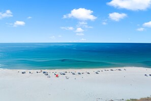 Ein Strand mit klarem, blauem Wasser, sandigem Ufer und einigen Strandsonnenschirmen.