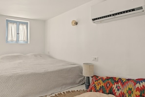 Une chambre à coucher avec un lit, une fenêtre avec des rideaux, un climatiseur fixé au mur et une lampe.