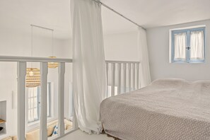 Een slaapkamer met een bed, een raam met gordijnen, een balkon met een leuning en een hanglamp.