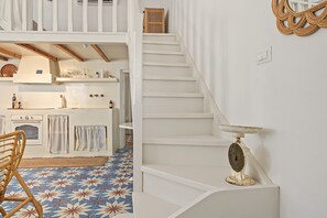 Een trap met een antieke weegschaal op de overloop, een keuken met een patroon vloer en een stoel met een geweven zitplaats.