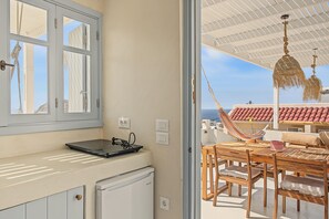 A room with a view of the sea, a dining area with a table and chairs, and a hammock.