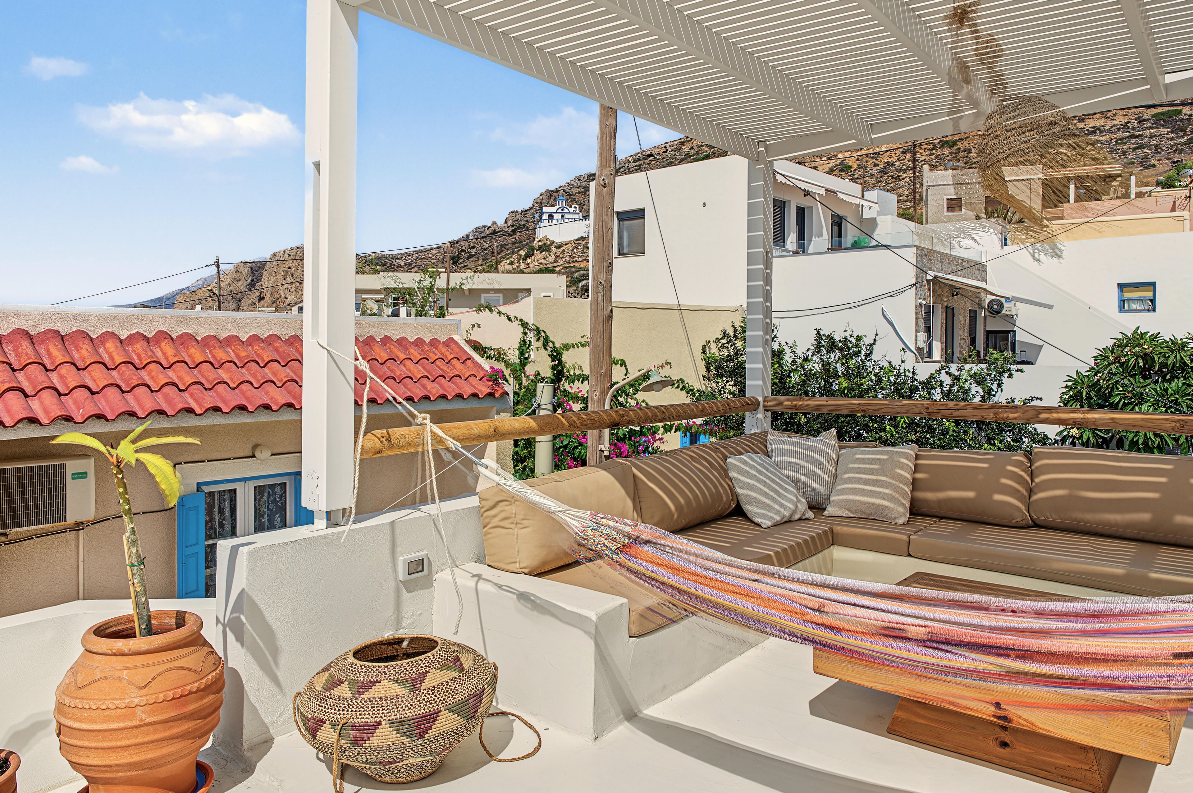 A rooftop terrace with a hammock, a sofa, terracotta pots, and a view of the surrounding buildings.