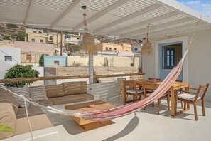 Een terras met een hangmat, houten meubels en uitzicht op de stad.