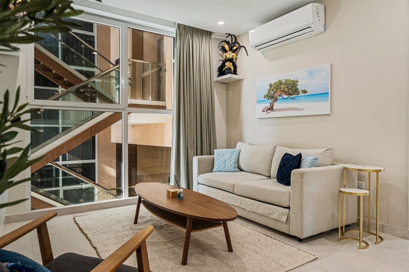 A modern living room with a sofa, coffee table, and a painting of a tree by the sea.