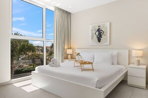 Ein modernes Hotelzimmer mit einem großen Bett, Blick auf Palmen und einem Gemälde an der Wand.