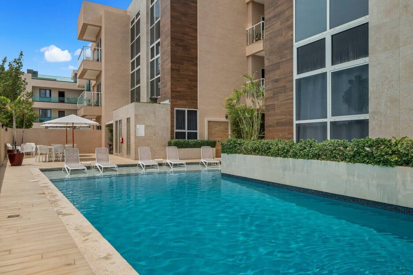 Ein Swimmingpool mit Liegestühlen und einer Holzterrasse, umgeben von modernen Gebäuden mit Balkonen.