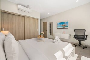 Quarto de hotel com cama, escrivaninha, cadeira, TV e um quadro na parede.