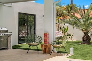 Eine Terrasse im Freien mit zwei grünen Stühlen, einem Grill und einem kleinen Baum.
