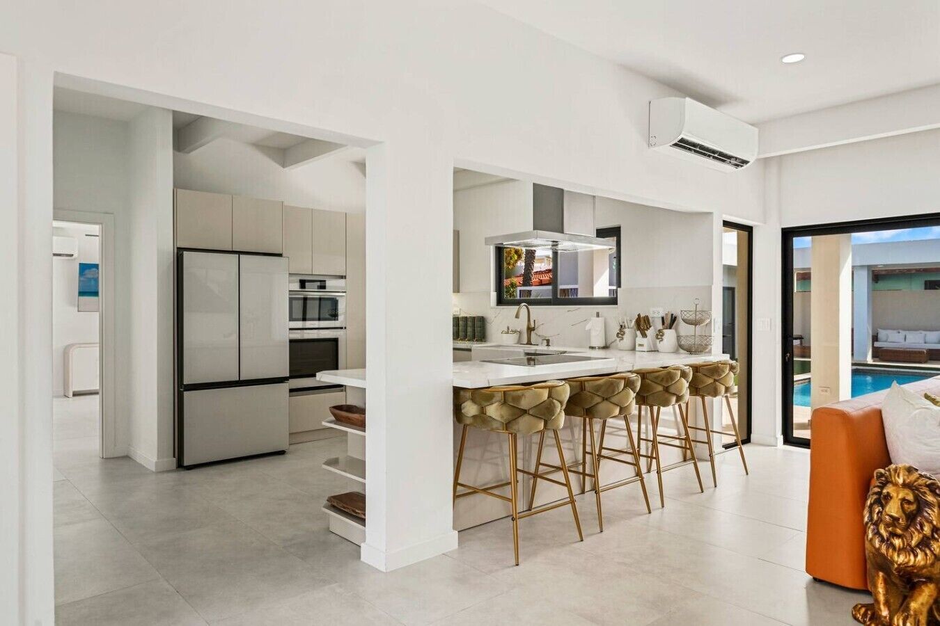 Una cocina moderna con una isla central, taburetes de bar y vistas a una piscina.