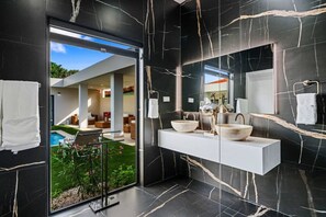 Ein modernes Badezimmer mit großem Spiegel, zwei Waschbecken und einer Glastür zum Poolbereich.