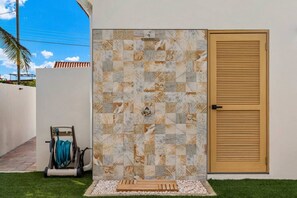 Eine Tür mit steinverziartem Mosaik, daneben eine Holztür und links ein Gartenschlauch.