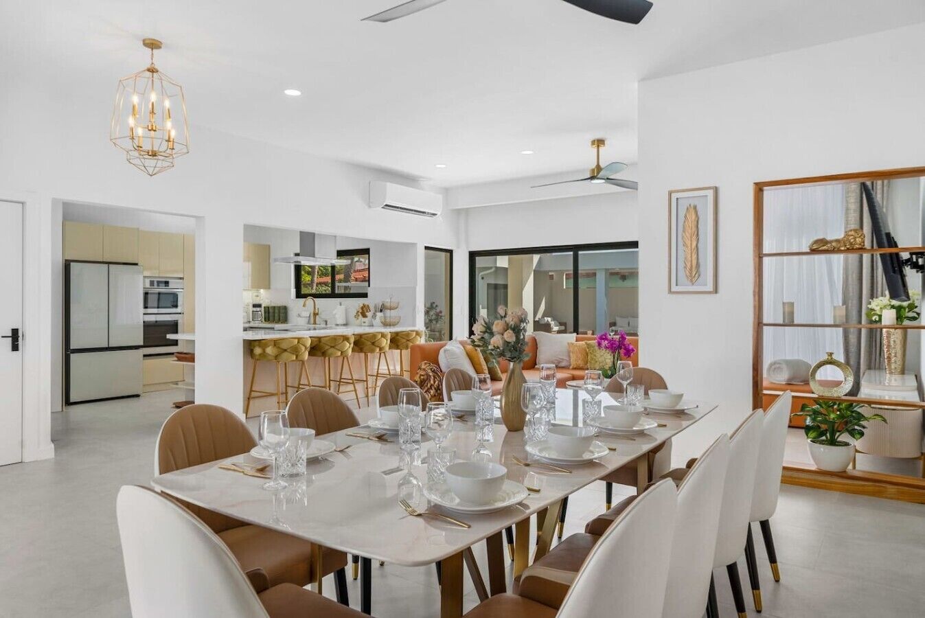 Un comedor moderno con una mesa larga dispuesta para seis personas, una cocina al fondo y un espejo grande que refleja la habitación.