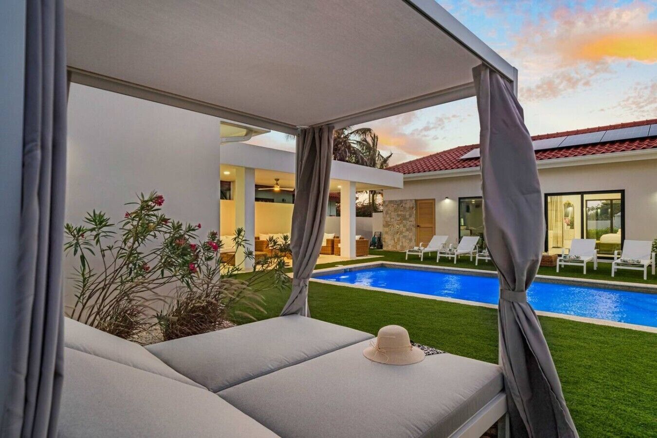 Zona junto a la piscina con vista a una casa, un espacio de descanso cubierto y un sombrero sobre un cojín.