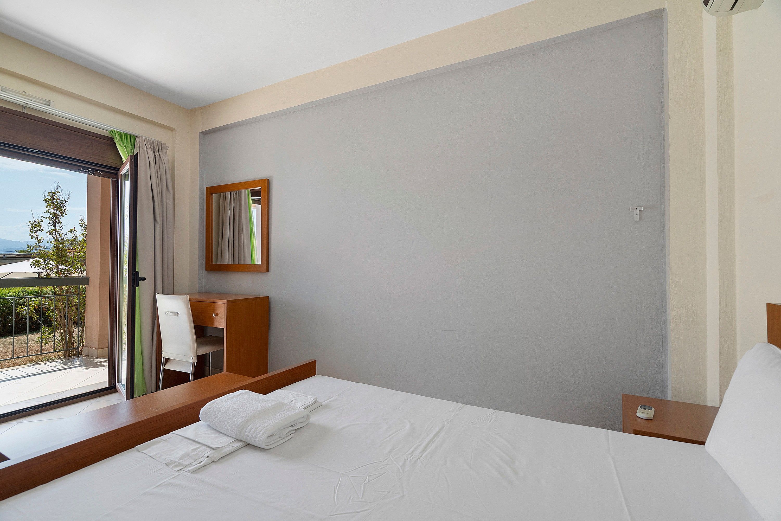 A hotel room with a bed, a desk, a chair, a window with a view, and a mirror on the wall.