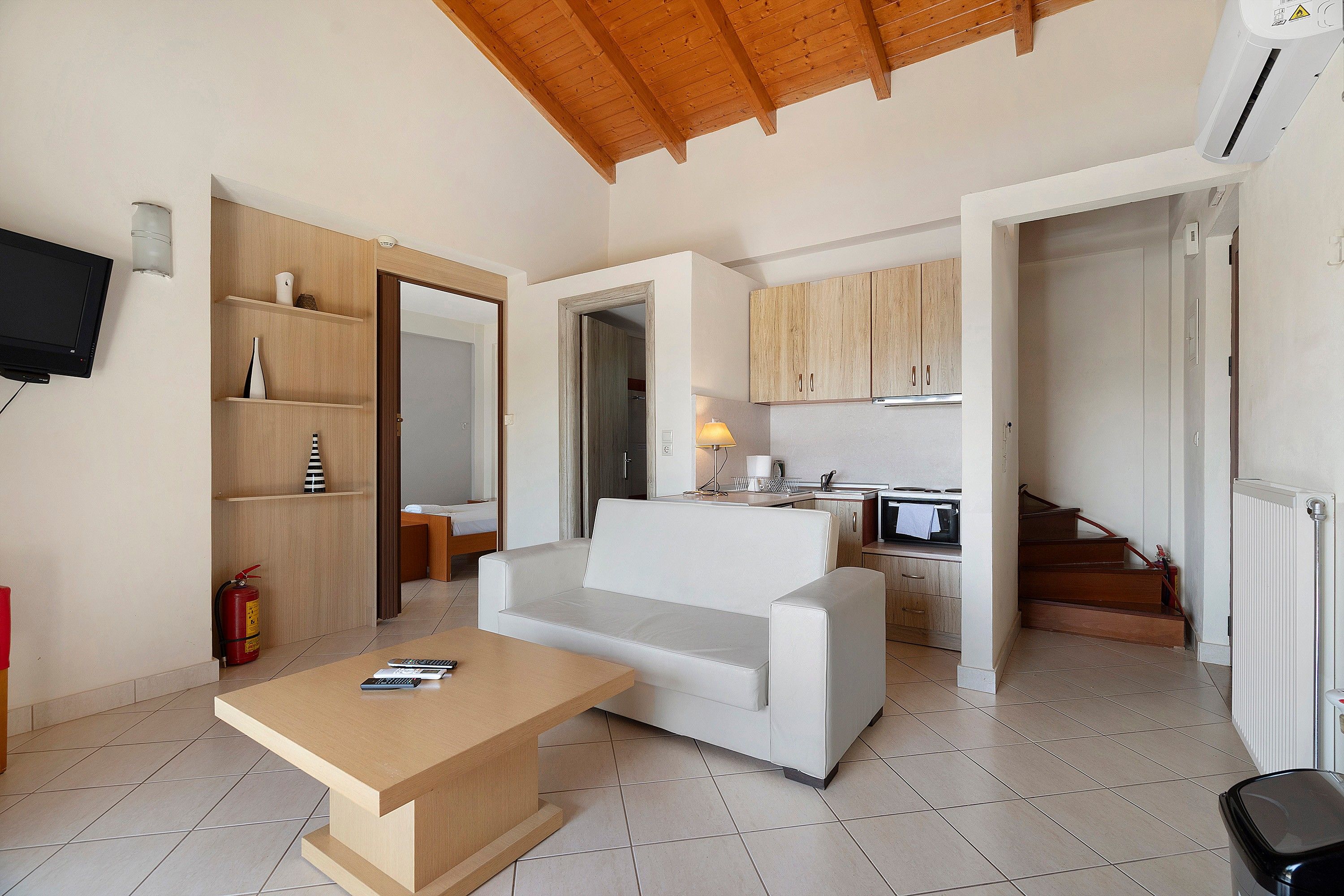 A compact living space with a sofa, a coffee table, a television, and a kitchen area with cabinets and a stove.