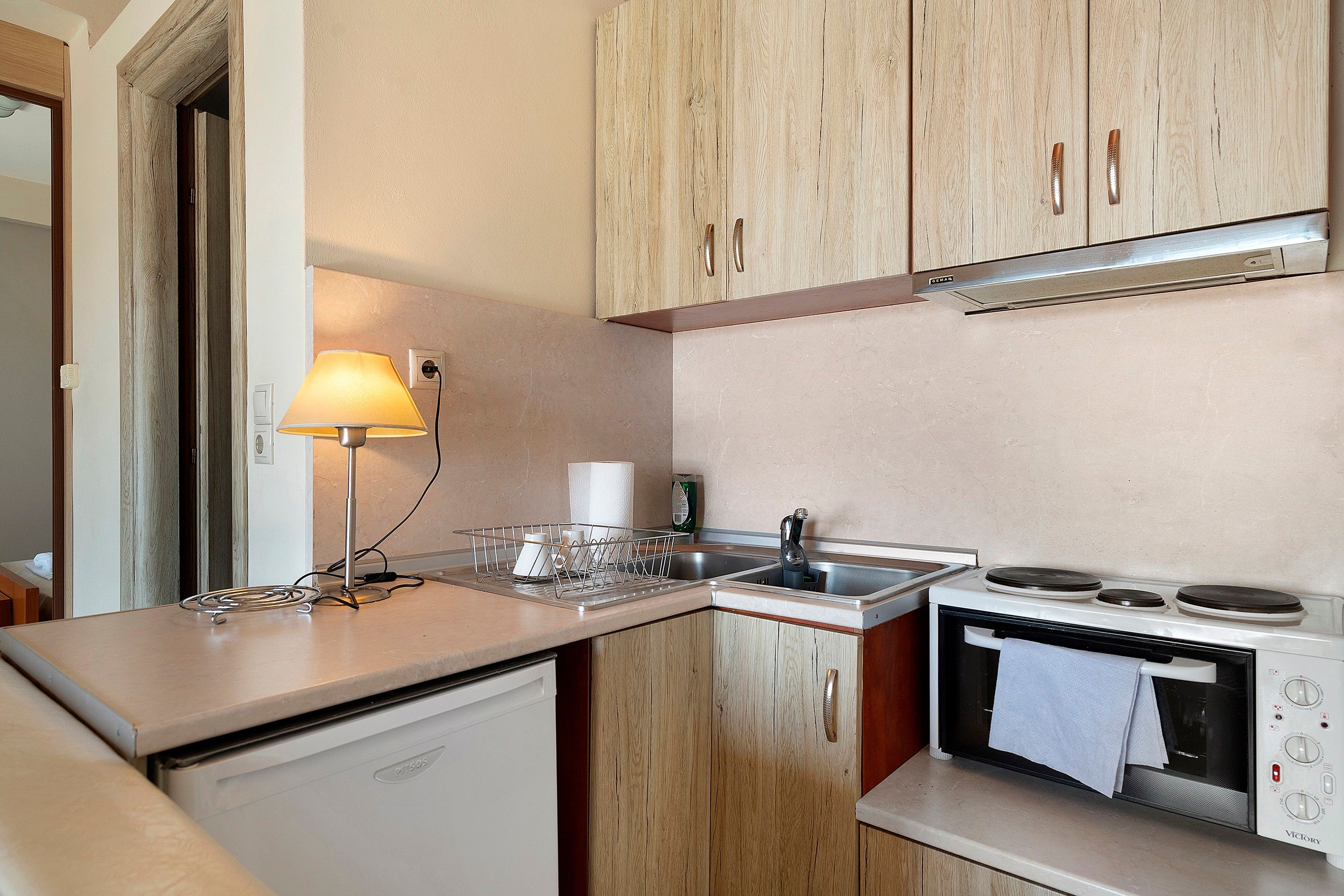 A compact kitchenette with wooden cabinets, a built-in microwave, a stove, and a small sink.