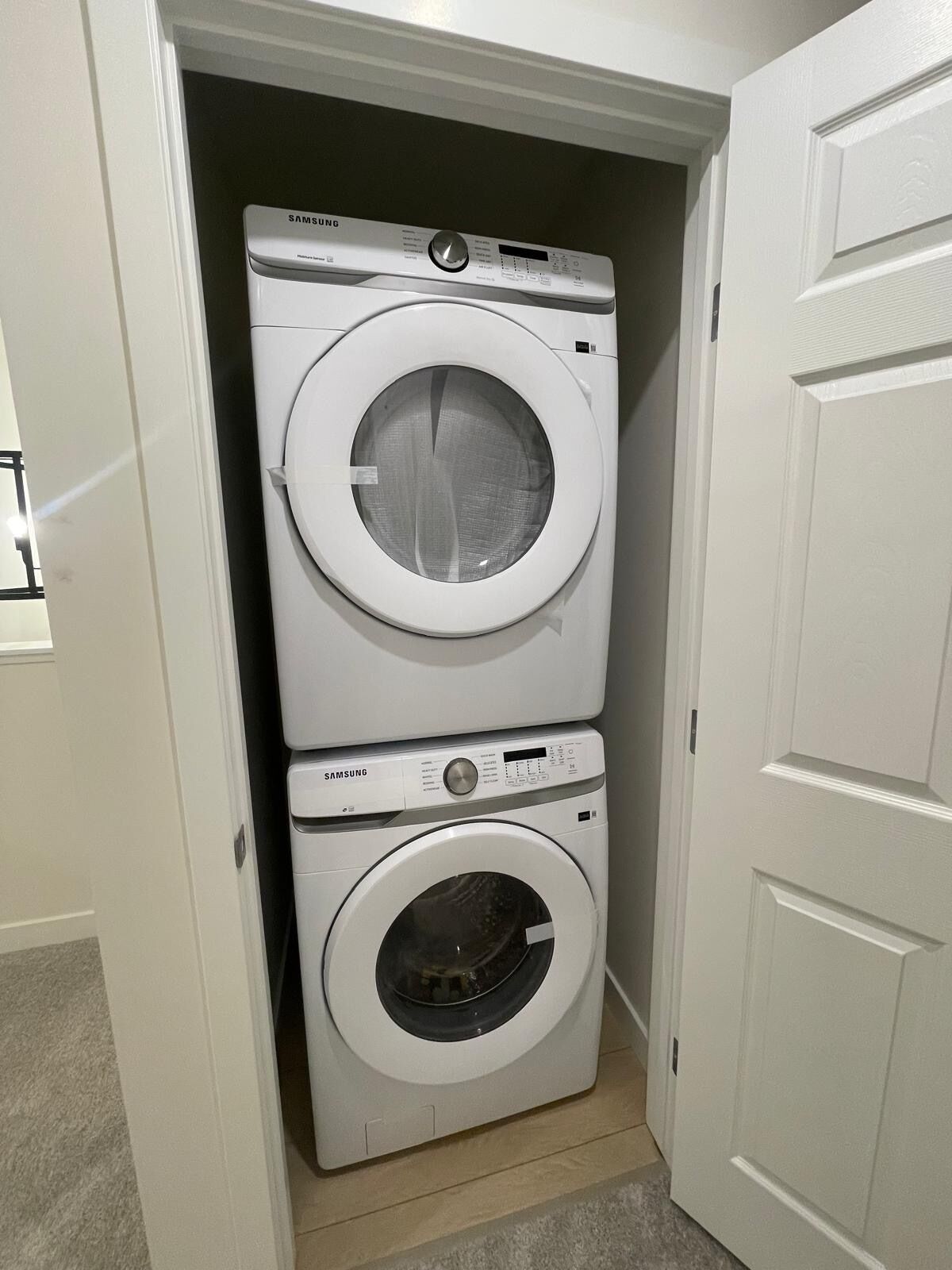 A laundry room with two stacked washing machines, one above the other, and a door leading to another room.