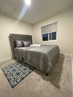 Ein Schlafzimmer mit einem Bett, einem Kopfteil, einem Fenster mit Jalousien und einem gemusterten Teppich.