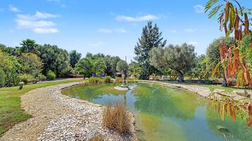 Jardim ajardinado com lago, cercado por diversas árvores e arbustos.