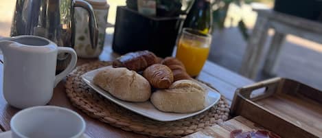 A breakfast setting with a coffee pot, croissants, a bottle of juice, and a plate of food on a wooden table.