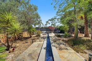 A garden pathway leading to a seating area with a pool, surrounded by various plants and trees. - Room 'The Courtyard' with Shared Pool, Shared Garden and Wi-Fi (Almancil)