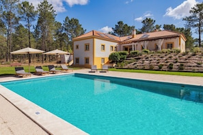 Ein zweistöckiges Haus mit Swimmingpool, umgeben von Bäumen und einer Rasenfläche mit Liegestühlen.
