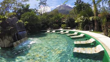 Une piscine aux eaux cristallines, agrémentée d’une cascade, entourée d’une végétation tropicale et avec une montagne en toile de fond.