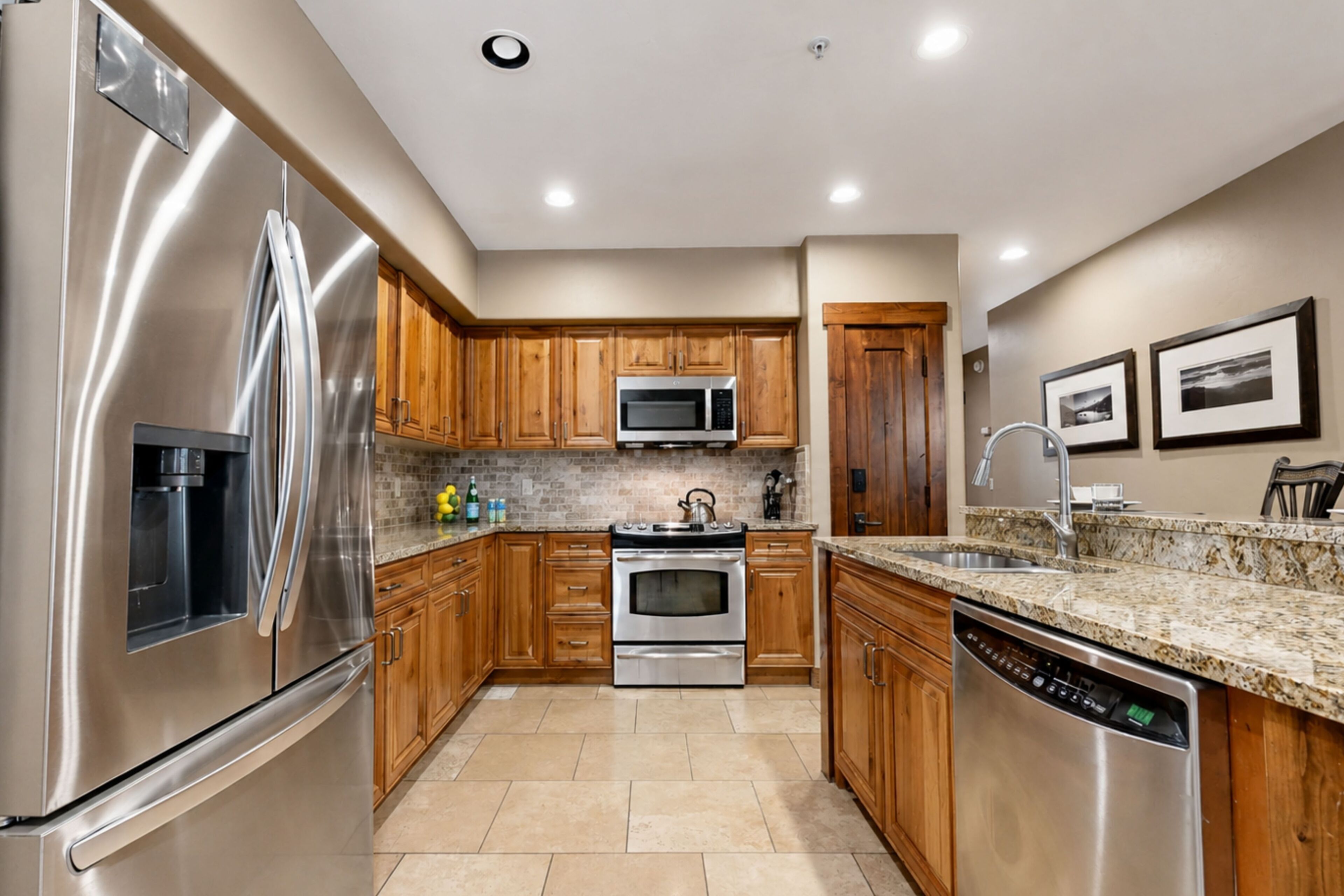 A modern kitchen with stainless steel appliances, wooden cabinets, a granite countertop, and a built-in dishwasher.