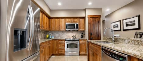 A modern kitchen with stainless steel appliances, wooden cabinets, a granite countertop, and a built-in dishwasher.