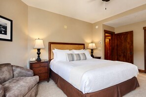 A bedroom with a large bed, two bedside tables with lamps, a wooden headboard, a framed picture on the wall, and a door leading to another room. - Crystal Peak Lodge 7403 ~ Ski-in/Ski-out ~ NEW LISTING ~ By CoralTree Residences (Breckenridge)