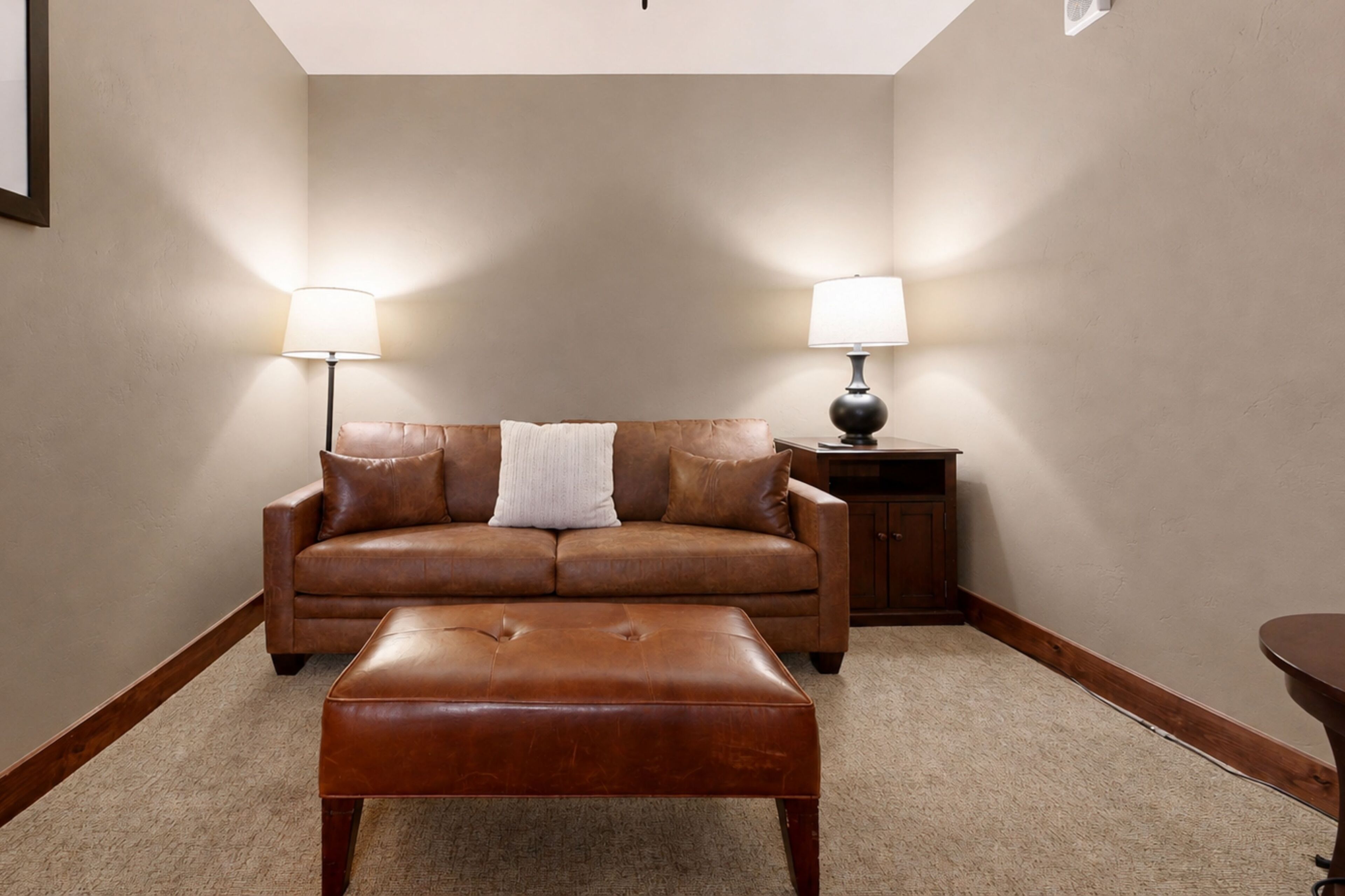 A living room with a brown leather sofa, a matching ottoman, and two floor lamps.