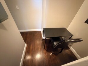 Una habitación de esquina con piso de madera oscura, una pequeña mesa negra y una pared blanca.