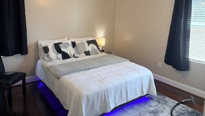 Une chambre à coucher avec un lit, un ventilateur de plafond, une table de chevet et une fenêtre avec des rideaux.