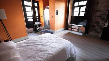 A hotel room with a large bed, a TV, a bathroom with a sink and mirror, and a brick wall.