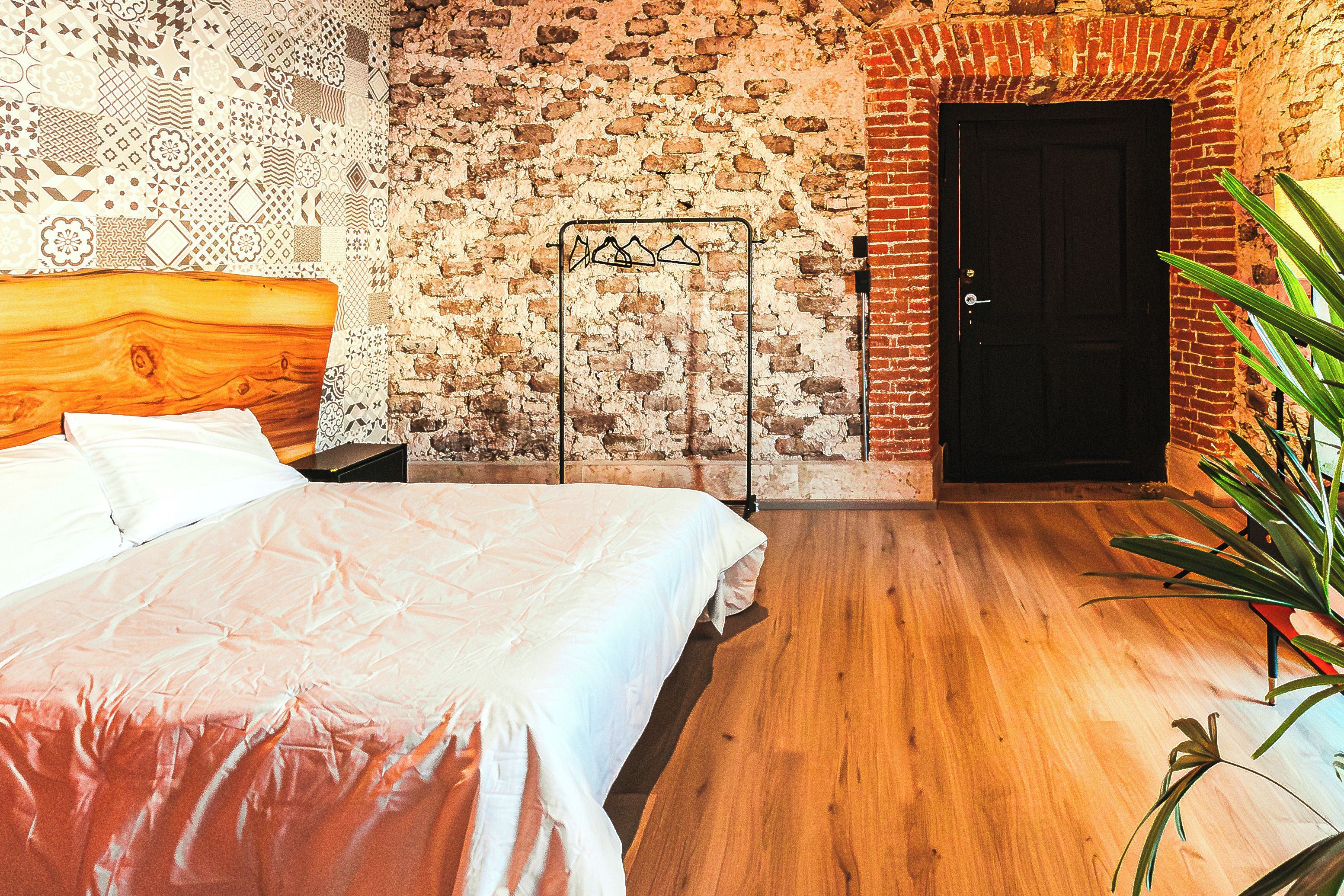 Een slaapkamer met een houten hoofdeinde, een bed met een witte spreideken, een bakstenen muur en een deur.