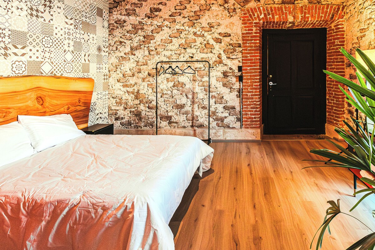 A bedroom with a wooden headboard, a bed with white bedding, a brick wall, and a door.