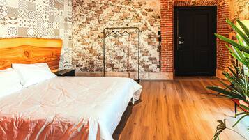Een slaapkamer met een houten hoofdeinde, een bed met een witte spreideken, een bakstenen muur en een deur.