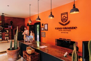 A hotel reception area with a wooden counter, a receptionist, and a large orange wall with the hotel's name and logo. - Casa Grande Rio (Rioverde)