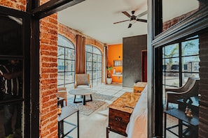 A room with a brick wall, large windows, a ceiling fan, and a wooden bench.